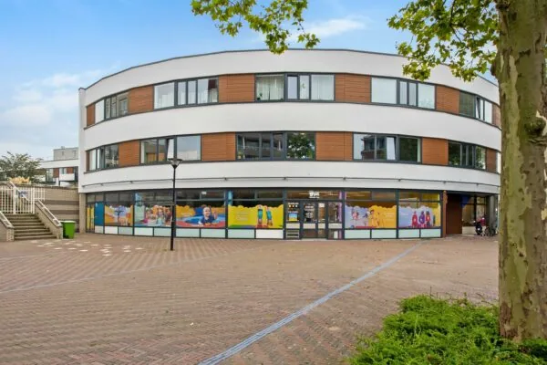 Modern rond gebouw aan de Koningin Julianalaan met kleurrijke raamstickers van een kinderopvang of sportschool.